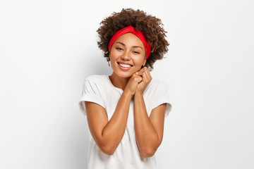 Photo of attractive young woman with Afro hairstyle, keeps hands pressed together, wears red...