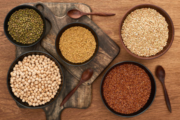 top view of bowls with moong beans, buckwheat and chickpea near spoons on wooden cutting boards