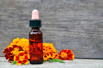 Marigold essential oil and fresh Tagetes flowers on old wooden background. Alternative medicine,aromatherapy or spa concept.Copy space.Selective focus.