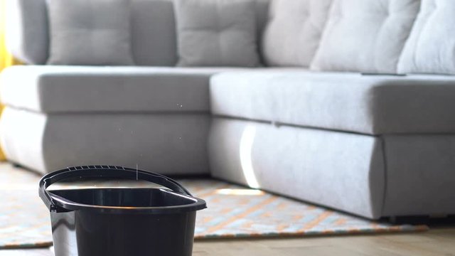Water dripping into bucket standing in living room floor, household destruction