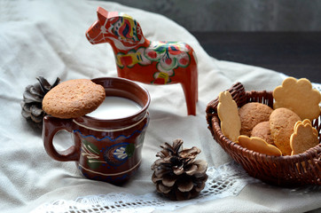cup of milk in clay cup with cookies standing on flax textile with decorations as Scandinavian horse Dalah&auml;st and  cones