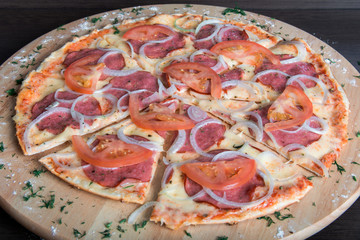 pizza with ham, onions and tomatoes on a wooden plate