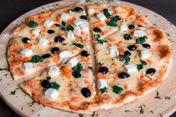 pizza with olives, cheese and spinach on a wooden plate