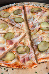 pizza with ham, pickles, onions on a wooden plate