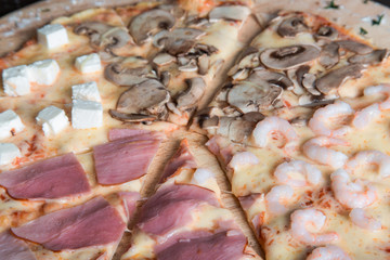 pizza with ham, feta cheese, mushrooms and shrimps on a wooden plate