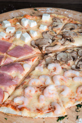pizza with ham, feta cheese, mushrooms and shrimps on a wooden plate
