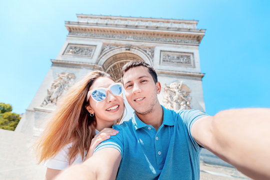 A happy man and a girl hug and take a selfie photo against the Arc de Triomphe in Paris. Honeymoon and a trip together in France