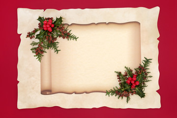 Holly berry and cedar cypress leaf sprigs on old scroll and parchment paper on red background. Document for a Christmas or winter theme.
