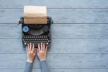 A woman hands is typing letter on a typewriter on blue wooden background with copy space.