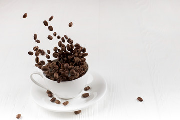 A cup with coffee beans in the air flying in flight like a spray. On background of a white wooden table, coffee shop advertising concept, copy space.