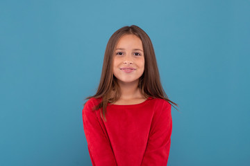 Half length portrait of a smiling young girl wearing red shirt against  blue background with copy space in studio.