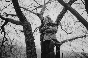 Black and white portrait of couple walking in the wilderness. Young people in love and lookin eye in eye, standing on the tree. Travel and tourism.