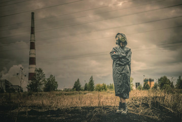 Woman in gas mask is standing on a smoking chimney background.