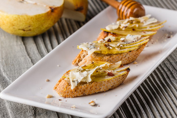 Appetizer bruschetta with pear, honey, walnut and blue cheese on white plate