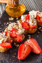 Bruschetta with strawberries, blue cheese, walnut and honey on stoyn plate