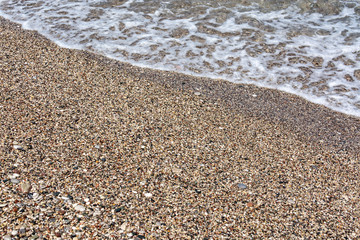 Sea water runs to the rocky shore and rolls, leaving a foamy trail. The next wave is already in a hurry to replace it.