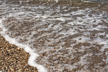 Sea water runs to the rocky shore and rolls, leaving a foamy trail. The next wave is already in a hurry to replace it.