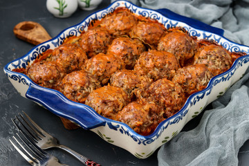 Meatballs in sour cream and tomatoes sauce in ceramic form against a dark background, horizontal orientation