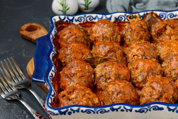Meatballs in sour cream and tomatoes sauce in ceramic form against a dark background, horizontal orientation