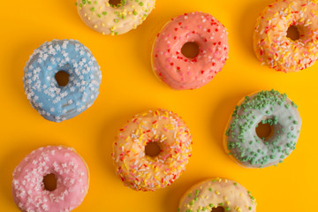Colored donuts, pastries on yellow background, top view.