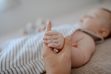 Close up of dad holding son's tiny hand. Baby lying on bed. Selective focus on hands.
