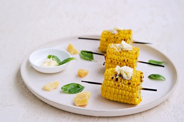 Grilled corn skewers on a white ceramic tray. Served with salted butter and grated Parmesan cheese. Vegetable dishes. Harvest the corn.