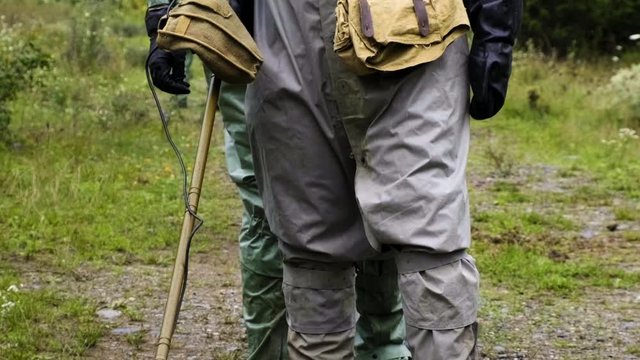 Three cadets of military men in a protective suit in a gas mask with a mine detector walk around Chernobyl in the forest
