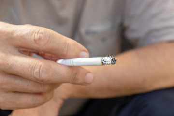 Man holding a lighted cigarette in fingers with a lot of ashes, bad habbits and nicotine addiction concept