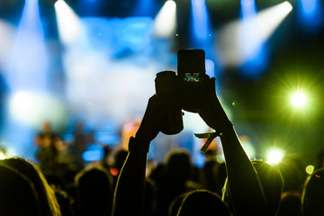 People taking photographs with smart phone during a public music concert with can of beer in hand