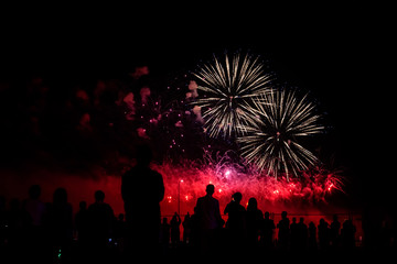 Fototapeta na wymiar silhouettes of people watching fireworks in the background of bright red flashes in the night sky