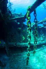 A decaying chain hangs from some structure in a sunken shipwreck. The rusting metal underwater provides a habitat for marine life and is also enjoyable for scuba divers to see