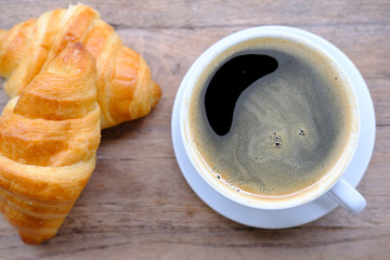 cup of coffee and croissant on wooden table