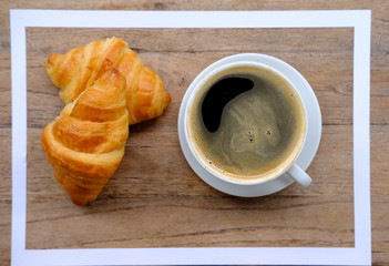 cup of coffee and croissant on wooden table