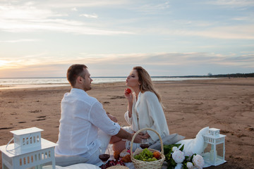 Picnic on the beach. A man and pregnant woman had a picnic. A woman holds a peach in her hand, a man touches her tummy.
