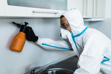 Exterminator in work wear spraying pesticide with sprayer. Selective focus.