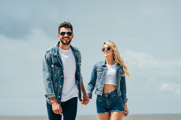 attractive woman and handsome man in denim jackets smiling and holding hands outside