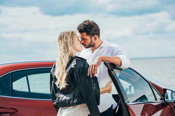attractive woman and handsome man kissing and hugging near car