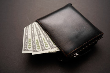 A wallet with dollar bills on dark background