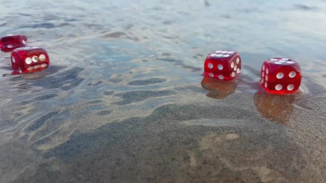A static footage at the beach showing a person picking and throwing red color ludo dice at the coast of a beach.Concept of Leisure,creativity,art,relaxation.