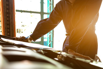 A mechanic service car in garage is check a list cars.