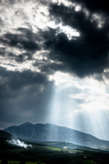 Dramatic sky with sunrays falling on mountain