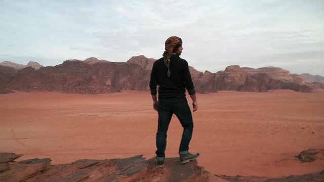 man standing on the edge of a cliff in the desert of wadi rum
