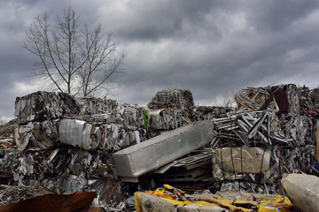 Heap of cubes of crushed recycled scrap metal with clouds and tree in Spring