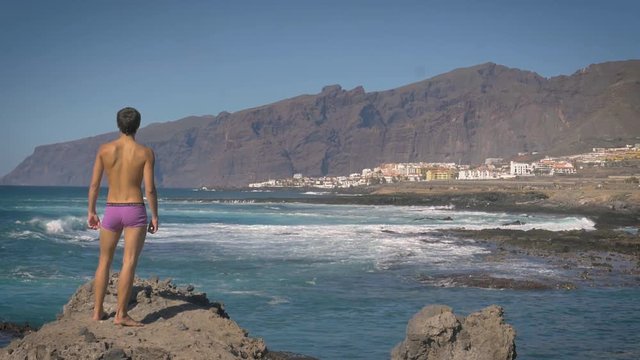 Man stands on a rocky outcrop while scanning the shoreline and surrounding mountains in Tenerife, Spain.