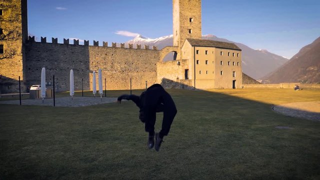 A young adult male makes a backflip on the grassy courtyard of the Grazzano Visconti castle. Slowmo. Full shot.