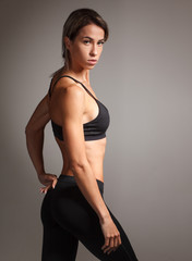 young muscular athletic sportswoman posing in sportswear on studio gray background