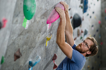 strong healthy active handsome man with beard wearing trendy glasses climbing on wall with color...
