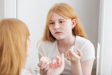 Obraz na płótnie Canvas teen girl examines acne in front of mirror