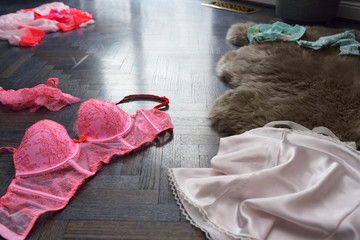 Hot pink womans undergarment lingerie strewn on a blue stained oak floor