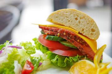 Corned beef slice in submarine sandwich with cheese, cucumber, tomato and lettuce salad on white plate